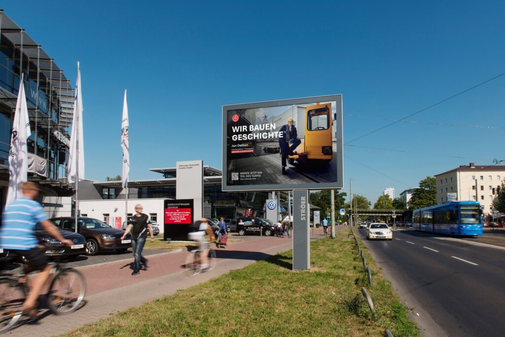 Eine Straße mit Fahrradfahrern, Passanten, blauen Himmel und einem Werbeplakat