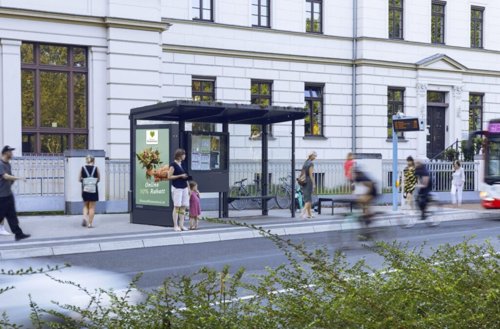 Mehrere Personen warten und gehen an einer hellen Bushaltestelle in der Stadt