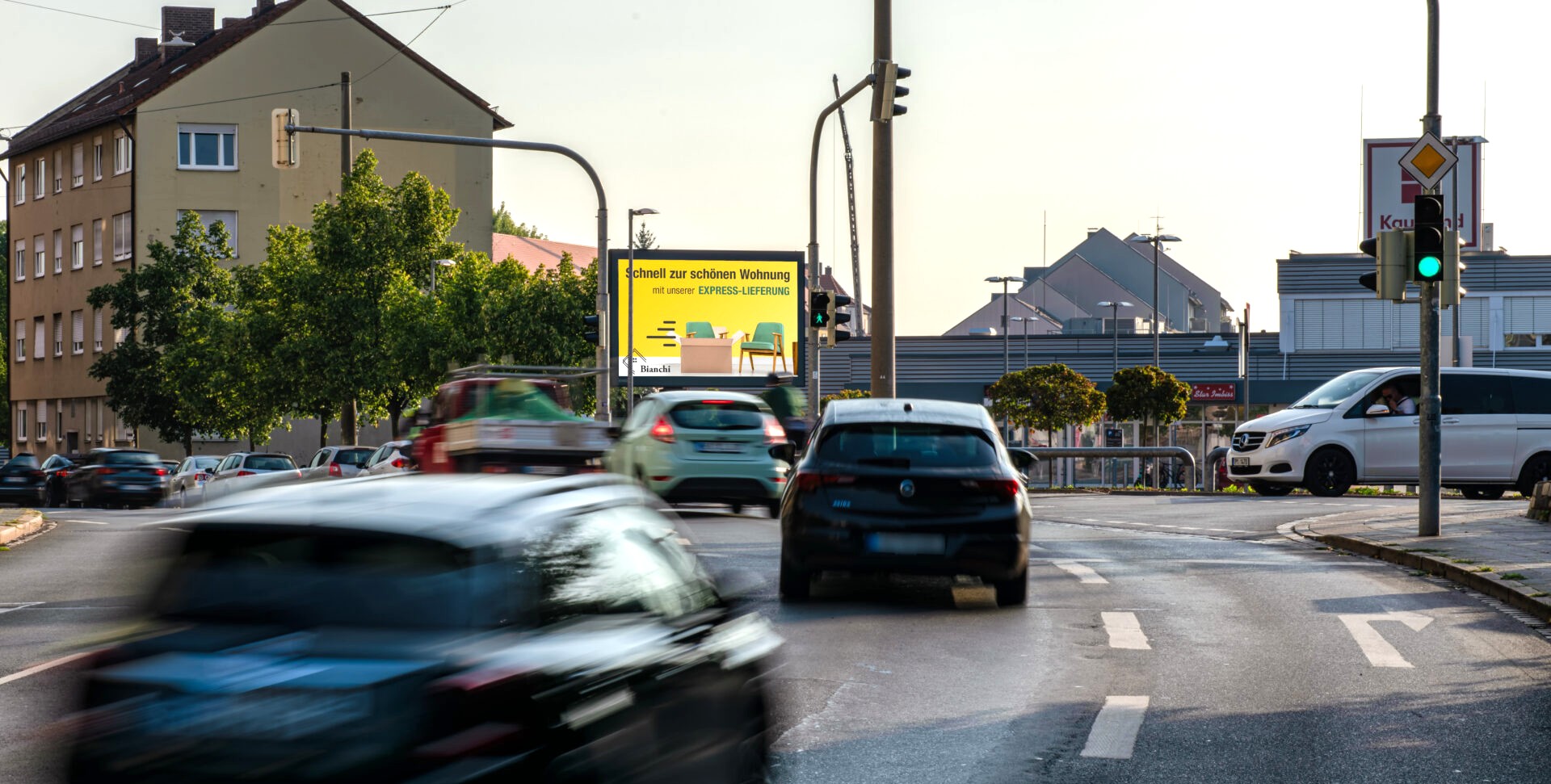 Verschiedene Autos fahren auf einer Stadtstraße bei Tageslicht mit Werbetafel im Hintergrund