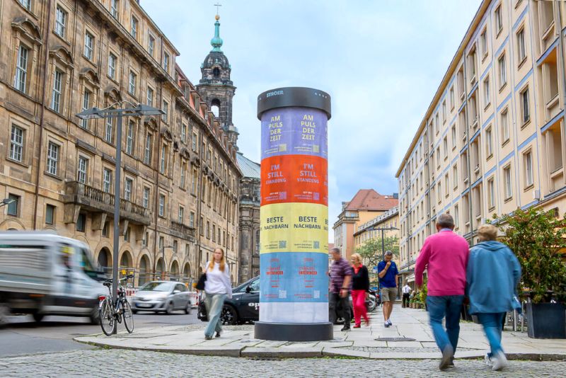 Mehrere Menschen spazieren entspannt über eine belebte Straße zwischen Altbauten