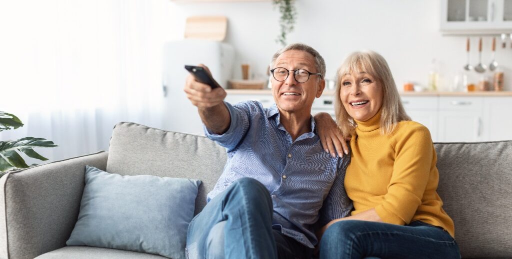 Happy Senior Spouses Watching TV Sitting And Hugging At Home