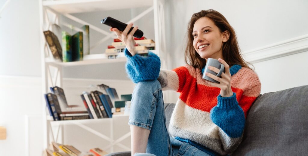 Photo of girl drinking coffee and using remote control while watching tv
