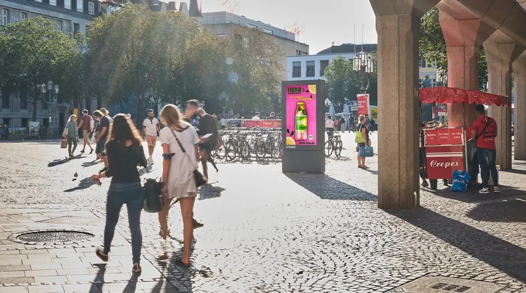 Zwei Personen gehen lächelnd über sonnigen Platz mit Radständern und Leuchtschild
