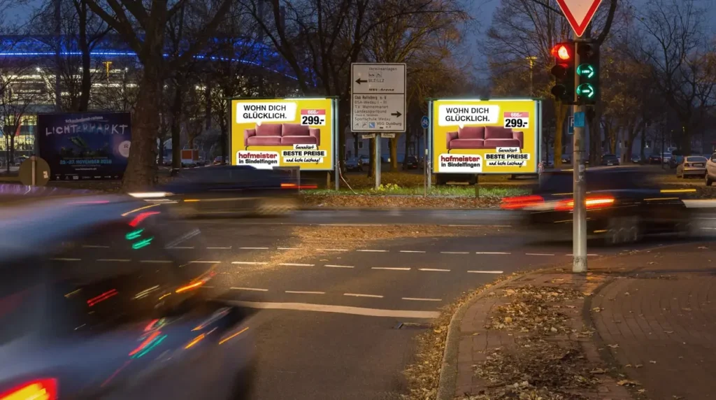 Nachtkreuzung mit schnellen Autos, gelben Werbetafeln und roter Ampel im Regen
