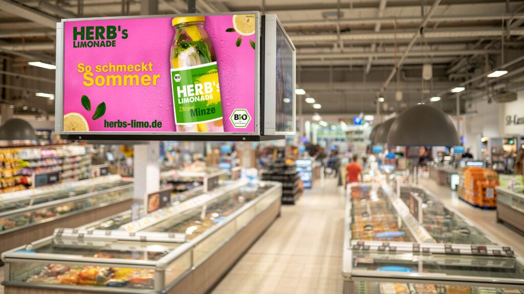 Werbetafel fuer Herbs Limonade in einem Supermarkt mit Kuehltruhen