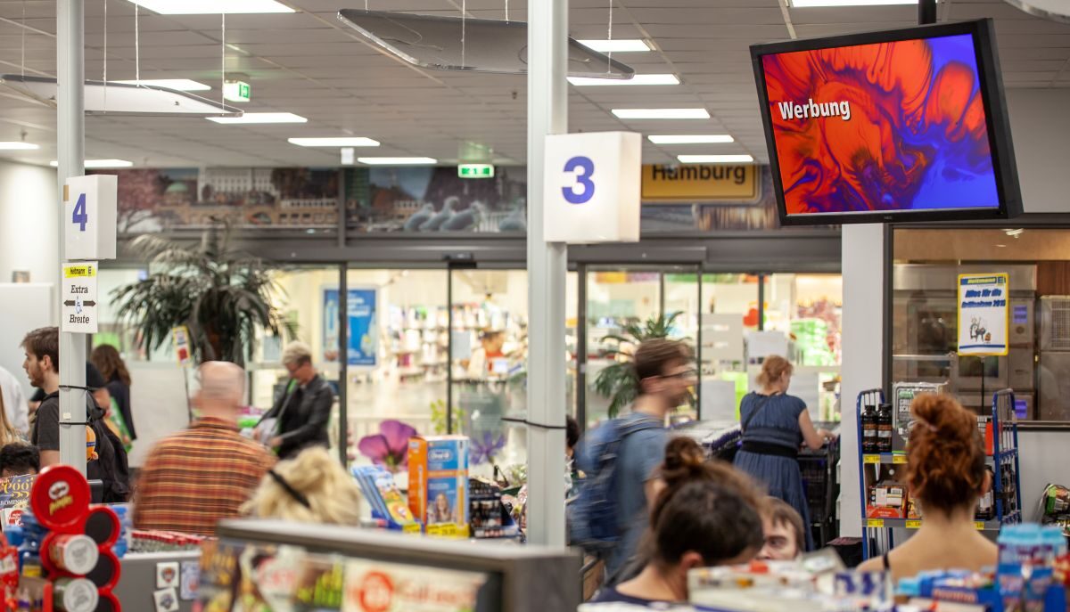 Kunden warten an den Kassen drei und vier in einem belebten Supermarkt