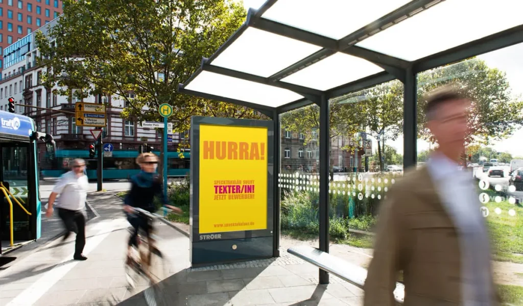 Gelbes Werbeplakat mit Aufschrift Hurra an einer Bushaltestelle in der Stadt