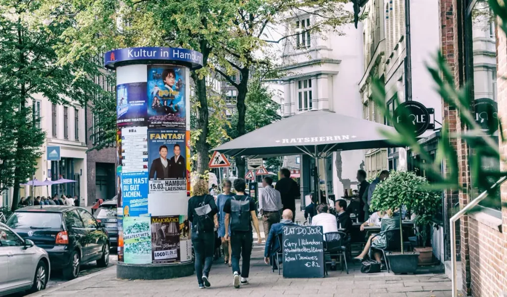 Belebte Hamburger Strasse mit Litfasssaeule Cafe und Passanten im Gruenen